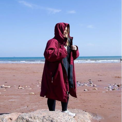 Person wearing a red hooded coat standing on a beach with blue sky and ocean.