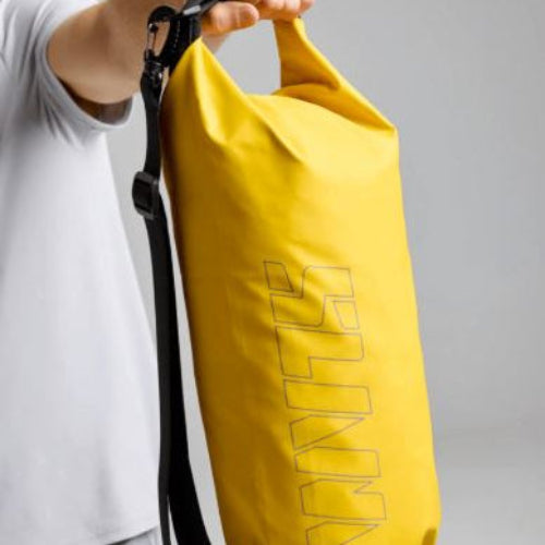 Yellow dry bag with a strap held by a person against a gray background